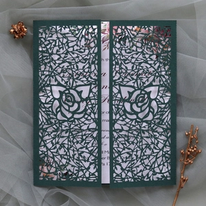 Detail of dark green laser-cut wedding invitation with intricate rose and vine patterns