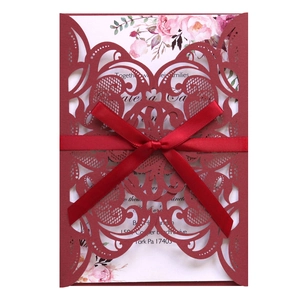 Detail of burgundy laser-cut wedding invitation with elegant floral insert and red silk ribbon