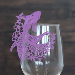 Close-up of laser-cut purple fish-shaped paper card used as a wine glass rim decoration