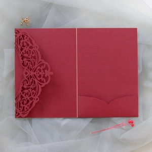 Detail of burgundy laser-cut invitation with intricate floral patterns and inner pocket card