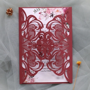 Detail of laser-cut burgundy lace wedding invitation with floral printed inner card