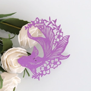 Close-up of laser-cut purple paper goldfish wine glass card with intricate floral patterns