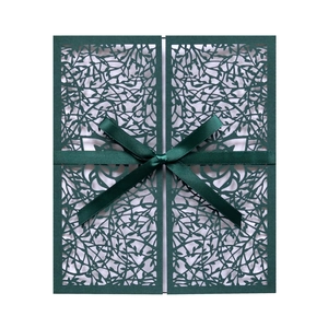 Close-up of laser-cut vine patterns on dark green wedding invitation with satin ribbon
