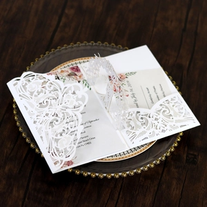 Close-up of laser-cut wedding invitation lace cover with floral inner card on glass tray