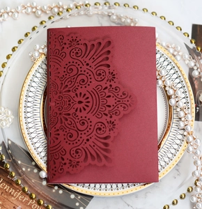 Detail of laser-cut burgundy wedding invitation with intricate floral hollowed patterns