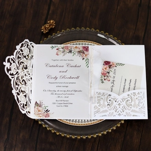 Detail of laser-cut ivory wedding invitation with floral insert and RSVP card set