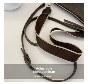 Detail van verstelbare lederen riem en brede canvas schouderband op een bruine handtas