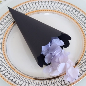 Macro view of a black scalloped edge paper cone filled with purple silk flower petals