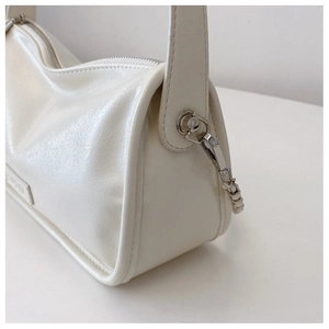 Detailed close-up of cream glossy leather handbag with silver metallic zipper and side buckle