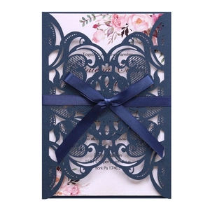 Close-up of laser-cut lace wedding invitation with navy blue ribbon and floral inner card