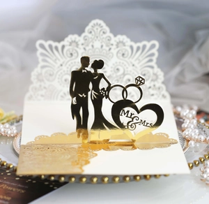 Detail of laser-cut gold wedding invitation featuring Mr & Mrs silhouettes and rings