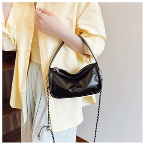 Detailed close-up of glossy black pillow bag with metal chain strap and leather tag