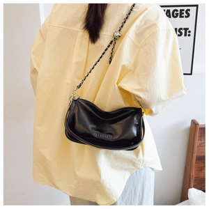 Model view of black glossy pillow bag with chain strap and branding detail