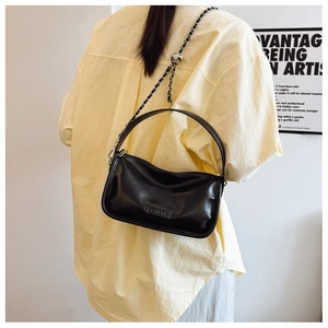 Detail view of black PU leather pillow bag with chain strap shown on a model