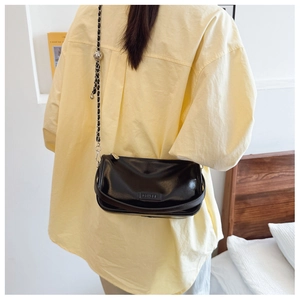 Detail of black crossbody bag featuring a metal chain strap and a silver ball pendant