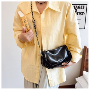 Classic black chain crossbody bag with glossy finish shown on model in a soft indoor setting