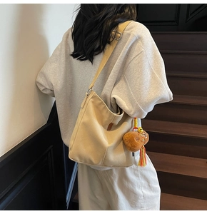 Détail du sac seau en toile beige avec breloque ours en peluche et pompon tissé