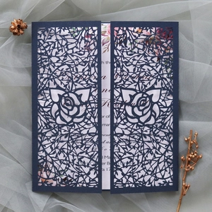 Detail of laser-cut navy blue wedding invitation with intricate rose pattern and white insert