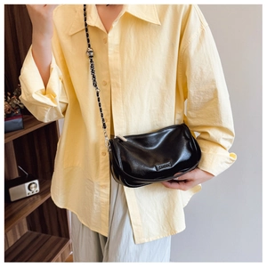 Chic black glossy leather pillow bag with chain strap shown on a yellow shirt