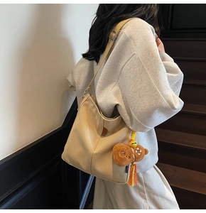 Détail du sac seau en toile beige avec un charm d'ours mignon et bandoulière ajustable