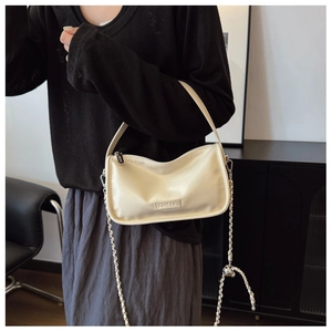 Detail of a creamy white leather handbag featuring a metal chain strap and logo embossed tag