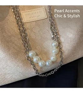 Detail of silver double-chain necklace with seven glossy white pearls on a beige bag