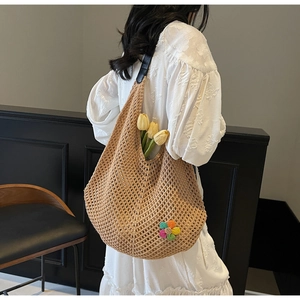 Close-up of hollow out woven shoulder bag featuring colorful floral detail and black leather handle