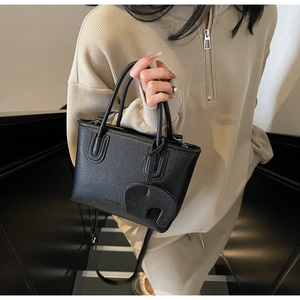 Detail shot of black litchi pattern leather bag with elephant charm and round top handles