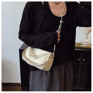 Detail of a creamy white crossbody bag with silver bead chain and metal logo plate