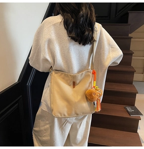 Détail d'un sac seau en toile beige avec pendentif ours porté par un mannequin