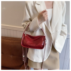 Detail of red wax leather crossbody bag featuring silver chain and embossed logo