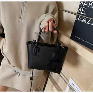 Detail of black lychee grain leather mini bag with semi-circular charm and shoulder strap