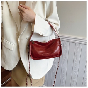 Detail of red glossy leather shoulder bag with silver chain strap and embossed logo