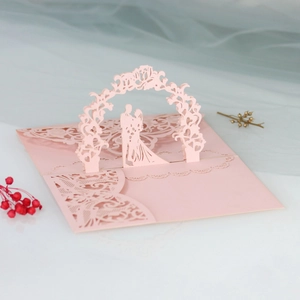 Detailed laser-cut 3D pop-up wedding invitation featuring a floral arch and pink bride and groom