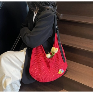 Red knit shoulder hobo bag with floral charm and black strap shown in a lifestyle setting