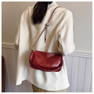 Model wearing a deep red textured crossbody bag with metal chain and silver ball detail