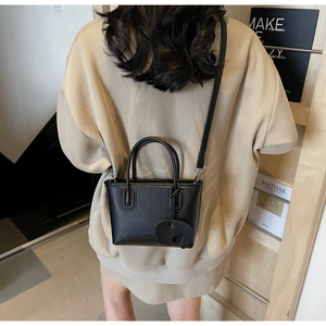 Detail of black lychee grain leather crossbody bag with cute elephant charm on model