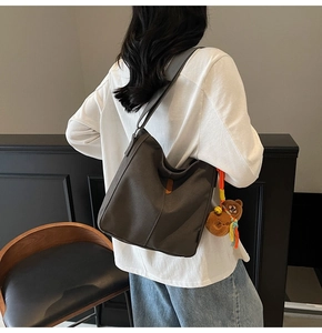 Détail d'un sac seau en toile gris foncé avec accent en cuir orange et charm ours en peluche