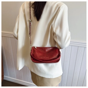 Detail of dark red leather crossbody bag featuring metal logo and chain strap on model