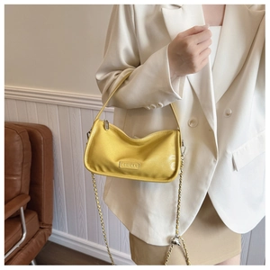 Detail of yellow glossy leather pillow bag with chain strap on a white suit model