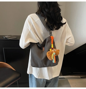 Détail du sac seau en toile gris foncé avec un pendentif ours brun et une étiquette en cuir
