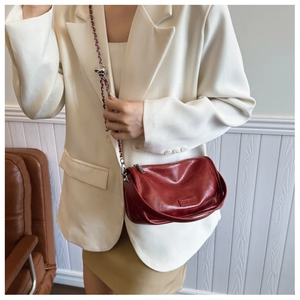 Detail of burgundy crossbody bag with metal chain strap worn with a white blazer