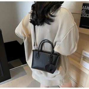Close-up of black litchi pattern mini tote bag with elephant charm on model back