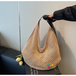 Detail of hollow woven straw tote with colorful crochet flowers and black leather handle