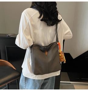 Détail du sac seau en toile grise avec un charm ours brun et l'étiquette en cuir JZBG
