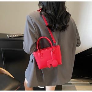 Detail of red lychee textured handbag with elephant charm and adjustable shoulder strap