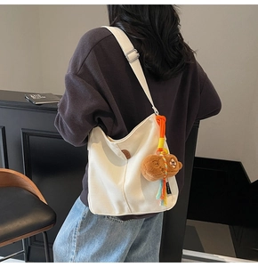 Gros plan détaillé d'un sac seau en toile blanche avec charm ours et logo en cuir