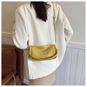 Close-up of yellow leather pillow bag with metal chain strap worn by a model