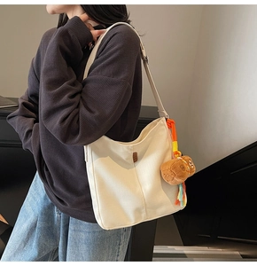 Détail du sac seau en toile blanche avec logo en cuir marron et pendentif ours en peluche