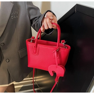 Detail of red lychee grain leather tote bag with elegant elephant charm and top handles